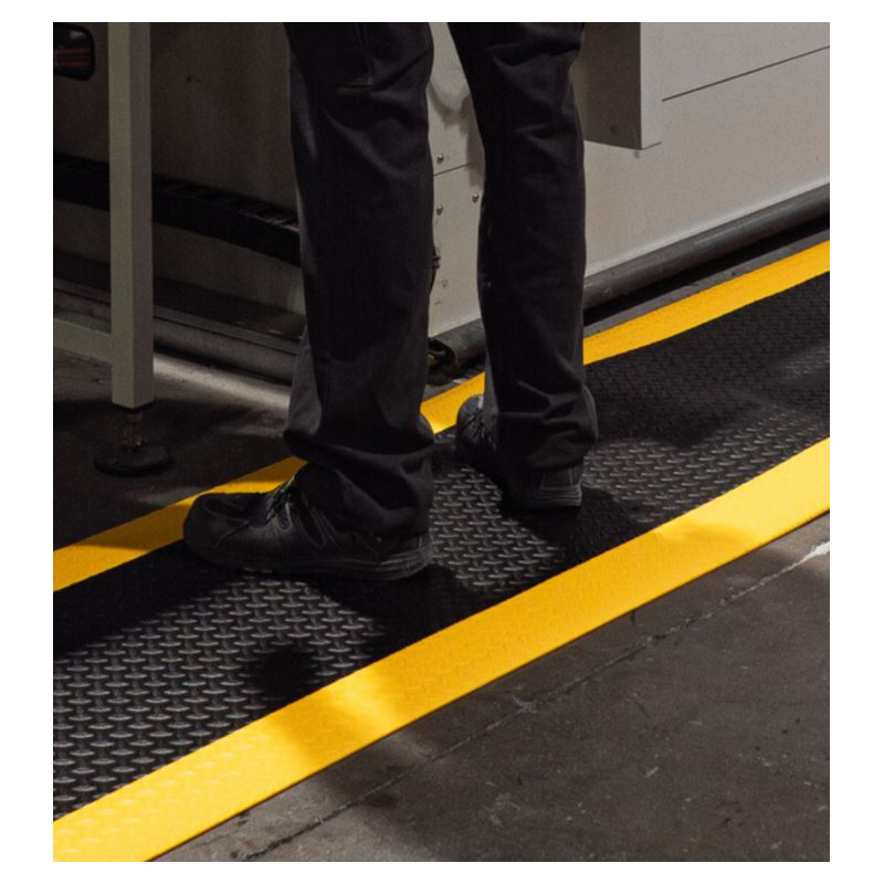 Opérateur en industrie utilisant le tapis antifatigue haute densité avec bandes jaunes pour un confort jusqu'à 8 h.