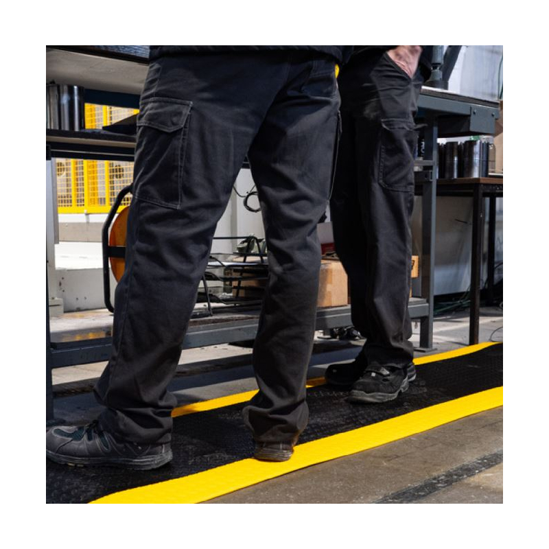 Focus sur la visibilité de la bande jaune de sécurité sur le tapis antifatigue en mousse haute densité.